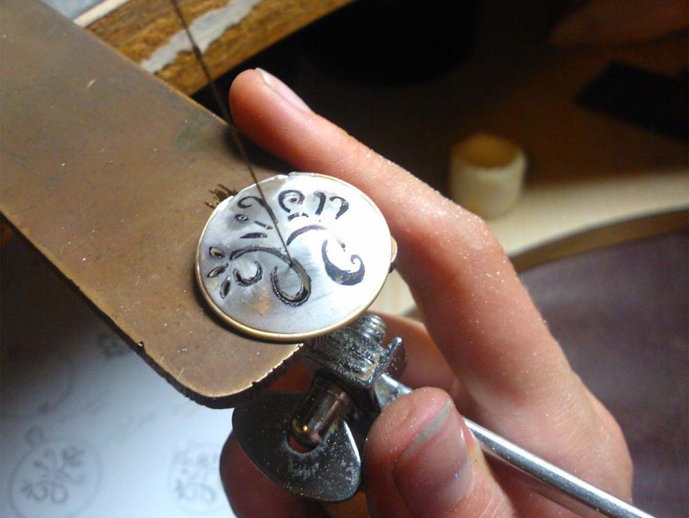 Jeweler using a saw frame and blade to cut and pierce sheet metal for jewelry making on a workbench